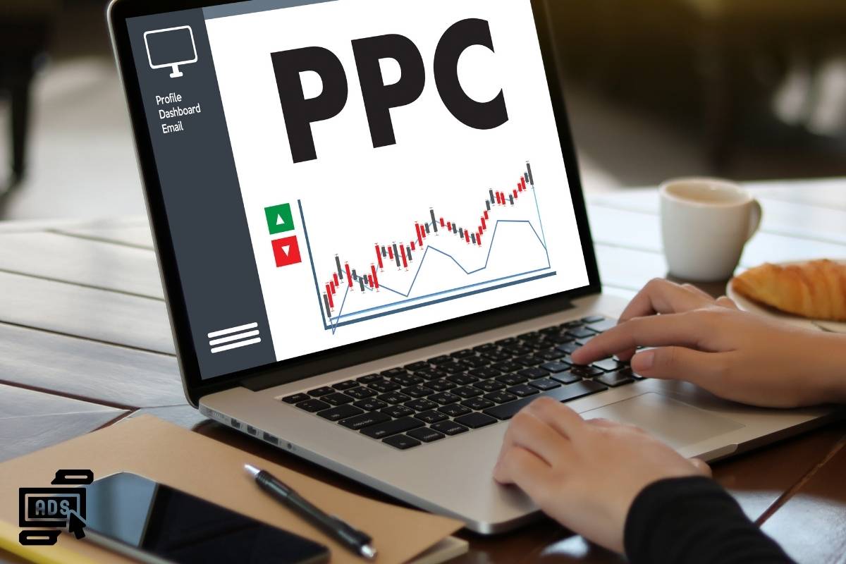 The image shows a person using a laptop with a screen displaying the term "PPC" in large, bold letters. Beneath it, there is a line graph with upward and downward arrows indicating trends or performance metrics. On the left side of the screen, there is a sidebar menu with options labeled "Profile," "Dashboard," and "Email." The person is typing on the keyboard of the laptop. In the bottom left corner of the image, there's an icon resembling a computer monitor with the word "ADS" written inside it, representing the concept of online advertising.