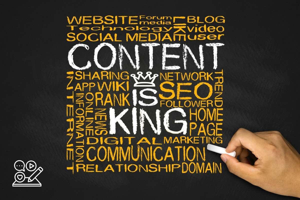 A chalkboard-style image with the phrase "Content is King" prominently displayed in white chalk in the center. Surrounding this central phrase are various related terms in different sizes and colors, including "Website," "Technology," "Social Media," "SEO," "Communication," "Digital Marketing," "Blog," "Trend," "Network," and "Relationship." A hand holding a piece of chalk is visible in the lower right corner, illustrating the writing of these words.